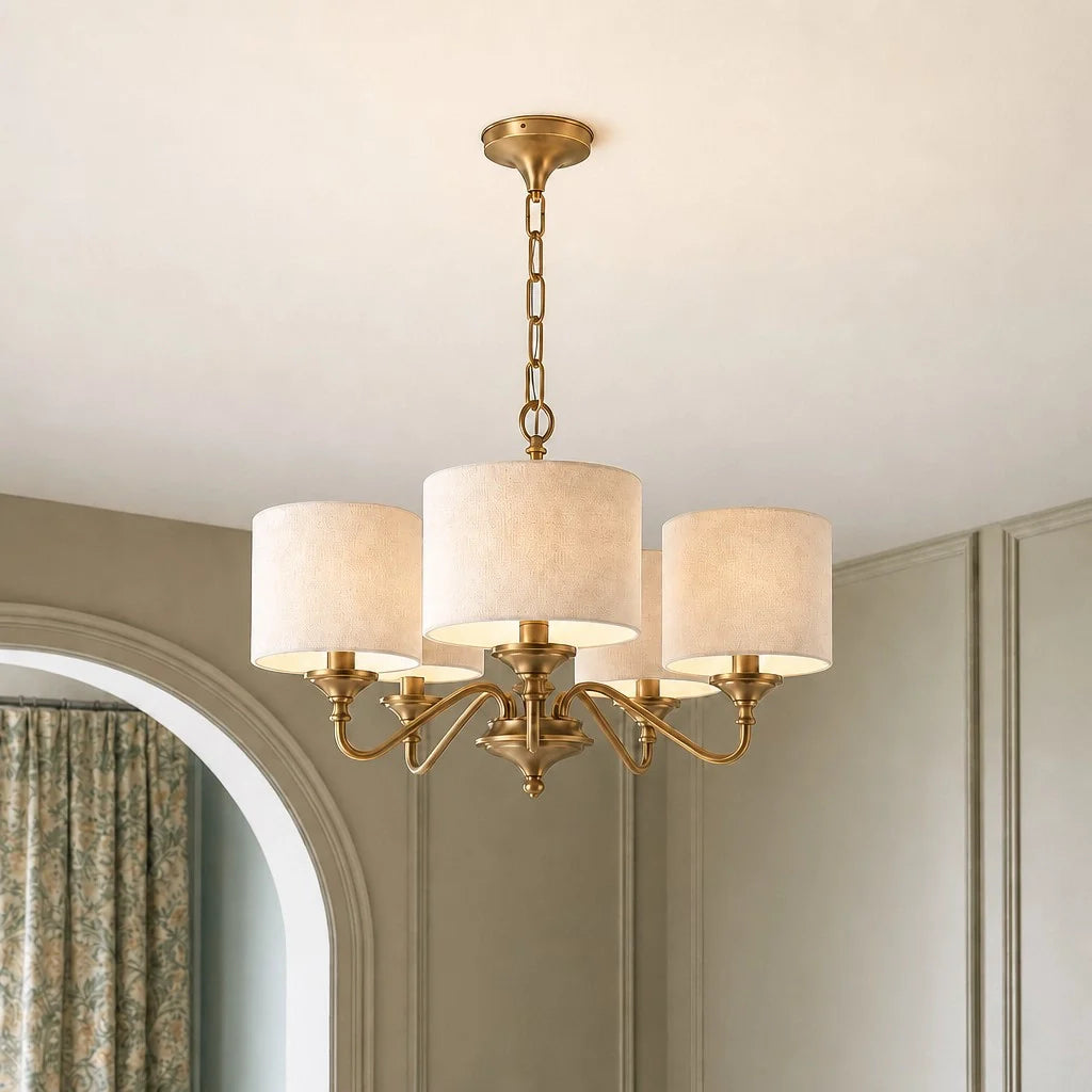 Gold chandelier with white lampshades hanging in a room with a mirror and curtain.