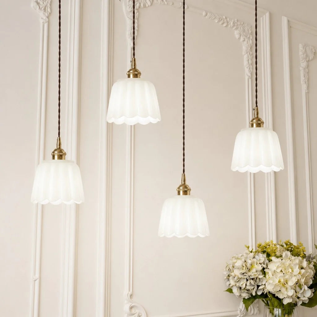 Four pendant lights with white glass shades hanging against a decorative wall.