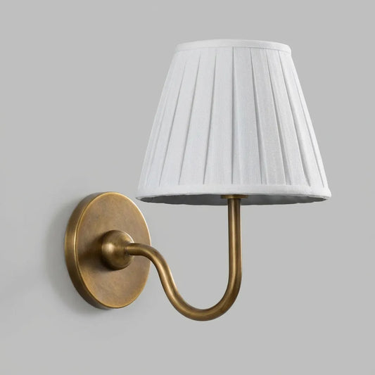Wall-mounted lamp with a white pleated shade and brass fixture on a gray background