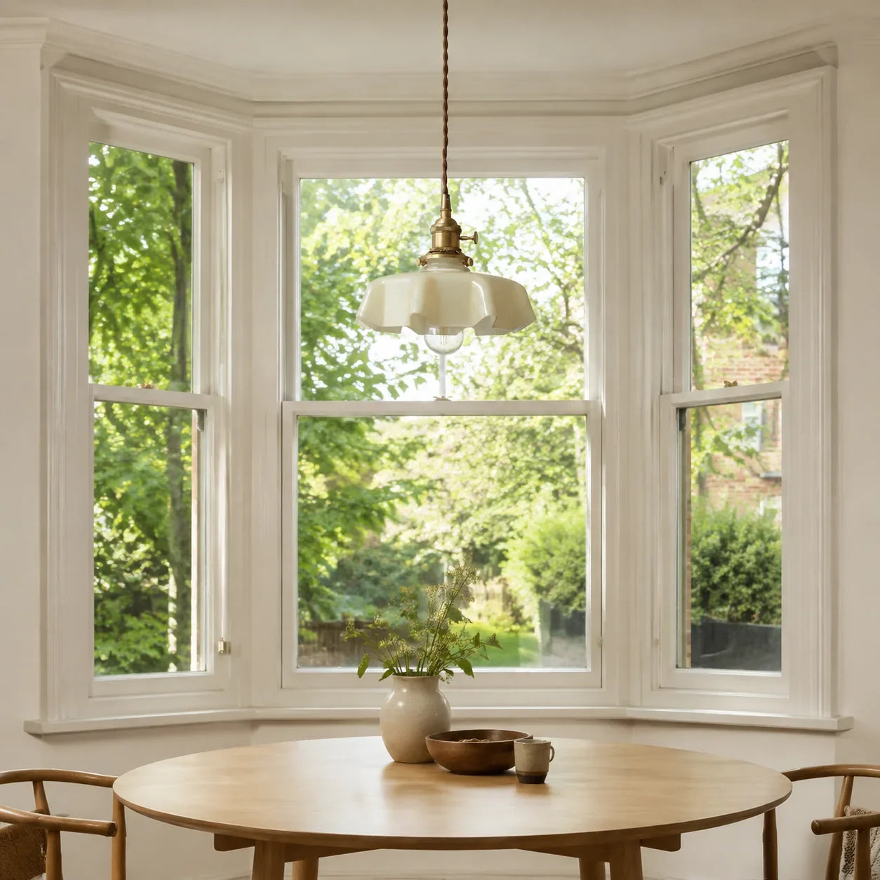 Cream Elowen pendant light above a round oak table in a bright British bay window